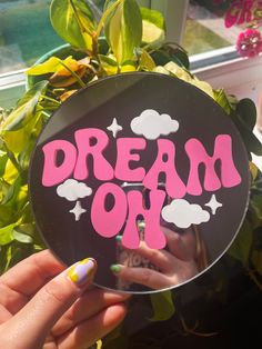 a person holding up a mirror with the words dream on it in pink and white