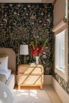 a bed room with a neatly made bed next to a night stand and flowers in a vase