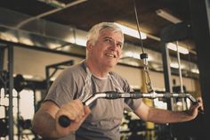 an older man working out in the gym with a barbell and pull up machine