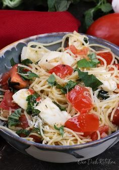 a bowl filled with pasta and vegetables on top of a table next to some tomatoes