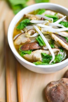 a white bowl filled with soup sitting on top of a wooden table next to chopsticks