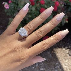 a woman's hand with a diamond ring on it and flowers in the background