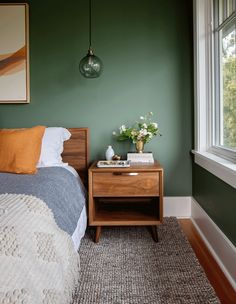 a bedroom with green walls and a wooden nightstand next to a bed in front of a window