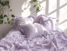 an unmade bed with white sheets and purple ruffled bedspread next to a potted plant