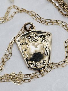 This is a "once in a lifetime" piece of estate jewelry.  This would make a lovely, thoughtful gift for your sweetheart. This very special antique locket necklace is made of highly polished solid yellow gold.  The locket is 10K and the chain is 14K.  Both are stamped accordingly. The locket has a unique shield shape which has a beautiful floral forget-me-not design on the front and a monogram on the back.  The locket is a little over one inch long.  The inside still holds the original black and white portrait of a handsome gentleman.  The photo is held in place by the original frame and cover.  I imagine there is a wonderful love story attached to this piece.  The necklace is a mini paperclip style chain with a spring ring clasp.  The clasp is stamped 585 (14K).  The chain is 18 inches long Vintage Charm Necklace For Mother's Day Anniversary, Vintage Charm Necklaces For Mother's Day Anniversary, Vintage Charm Necklaces For Anniversary And Mother's Day, Vintage Charm Heart Pendant Necklace For Anniversary, Anniversary Necklace With Vintage Charm And Heart Pendant, Vintage Charm Heart Pendant Jewelry For Mother's Day, Mother's Day Vintage Heart Pendant Jewelry, Vintage Charm Jewelry With Flower Pendant For Gift, Vintage Charm Flower Pendant Jewelry Gift