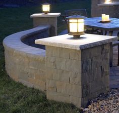 an outdoor table with two lit candles on it next to a fire pit in the grass