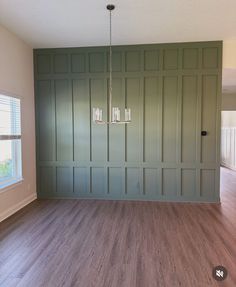 an empty room with wood floors and green painted walls, including a chandelier