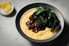 a bowl filled with mashed potatoes topped with meat and greens next to a glass of orange juice