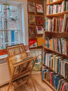 a bookshelf filled with lots of books in front of a window next to a desk