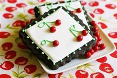 two decorated cookies sitting on top of a white and black plate with cherries around them