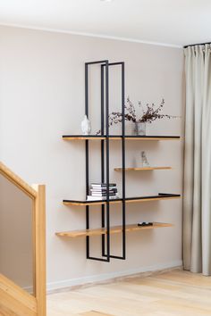 a book shelf with books and vases on it next to a curtained window