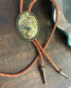 This awesome bolo tie has a southwestern design and genuine green/yellow jasper centerpiece. All stones will vary in grain/color. The cord is genuine brown leather with matching silver metal tips. Our bolos pair nicely with many of our belt buckles! They make wonderful gifts. The western bolo tie rope length is 40'' ; pendant size is 1 1/2'' x 1 1/4'' Western Lariat Jewelry As Gift, Western Style Lariat Jewelry For Gifts, Western Style Lariat Jewelry As Gift, Western Style Lariat Necklace For Gifts, Southwestern Bolo Tie With Sliding Knot, Handmade Western Lariat Jewelry, Handmade Lariat Bolo Tie For Rodeo, Southwestern Lariat Bolo Tie For Rodeo, Artisan Bolo Tie With Sliding Knot As Gift