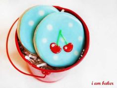 two decorated cookies in a red container with white polka dots and cherries on them