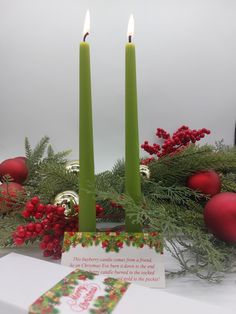 two green candles are sitting on a table with christmas decorations and red balls in the background