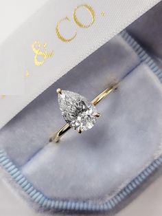 an engagement ring with a pear shaped diamond on it's side in a box