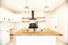 a kitchen with white cabinets and wood counter tops, an island sink and two hanging lights