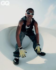 a man in black shirt and yellow gloves sitting on top of a white wall with his hands up