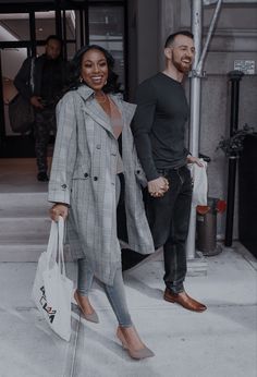 a man and woman holding hands while walking down the street with shopping bags in hand