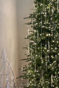 a white christmas tree with lights and ornaments on the floor next to a small glass cone