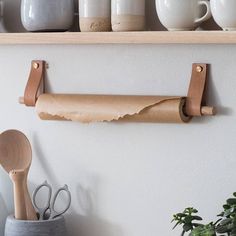 a shelf with some cups and utensils on it, next to a wall mounted toilet paper roll holder