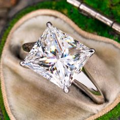 a white diamond ring sitting on top of a piece of cloth next to a pen