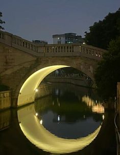 an arched bridge over a river at night with lights reflecting in it's water