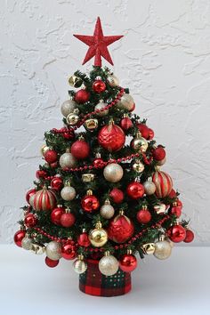 a small christmas tree with red and gold ornaments on it's top, in front of a white wall