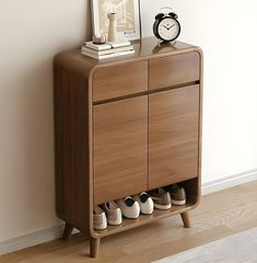 there is a small cabinet with shoes on it next to a wall and a clock