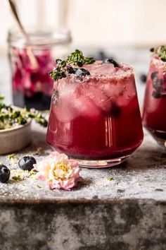 two glasses filled with blueberry lemonade sitting on top of a stone table next to flowers