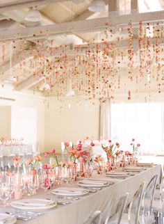 a long table is set with pink and white flowers in vases hanging from the ceiling