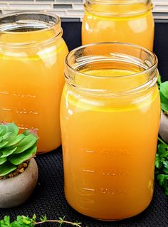 three jars filled with orange liquid sitting on top of a black table next to plants