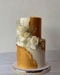 a three tiered cake with gold and white flowers on the top, sitting on a plate