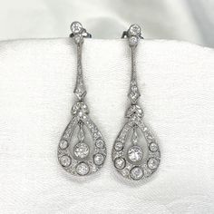 This lovely pair of earrings is Edwardian inspired, featuring intricate details in handcrafted platinum. Old mien cut diamonds are set along the drop of the earrings, surrounding the center diamond. The total approximate weight of these earrings is 2.00 carats. ✦ EARRING SPECIFICATIONS: Ring Material: Platinum Ring Era: Edwardian Era Stones: Diamond ✦ WHAT COMES IN YOUR SHIPMENT: - Your Engagement Ring - Quality Ring Box - Jewelry Cleaner - UGL Certificate ✦ WHY SHOP WITH US: - We've been in bus Exquisite Hallmarked Bridal Earrings For Formal Occasions, Elegant White Gold Earrings With Intricate Design, Exquisite Pierced Diamond Earrings For Formal Occasions, Exquisite Diamond Pierced Earrings For Formal Occasions, Elegant Teardrop Diamond Earrings Hallmarked, Exquisite Filigree Earrings For Formal Occasions, Exquisite Bridal Earrings For Formal Occasion, Exquisite Formal Bridal Earrings, Fine Jewelry Hallmarked Bridal Drop Earrings