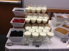 a table topped with lots of glasses filled with milk and berries next to bowls of cereal