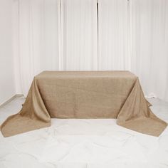 a table covered with a beige cloth in front of white curtains