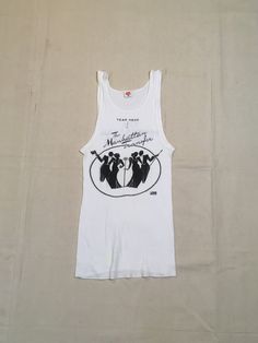 "1970s band tanktop shirt Hanes, cotton, white ribbed The Manhattan Transfer black print Atlantic Records symbol at lower right of image front/back image good vintage condition, light wear light stains, light cracking label size M, see below measures, lying flat, chest-12\" unstretched to 19\" stretched length-26\"" Fitted Sleeveless Cotton T-shirt, Retro Fitted Racerback Tank Top, Retro Racerback Tank Top With Graphic Print, Retro Racerback Top, Retro Fitted Racerback Top, Fitted Racerback Vest With Graphic Print, Fitted Retro Racerback Top, Retro Stretch Tank Top With Graphic Print, Vintage Tank Top For Spring Streetwear