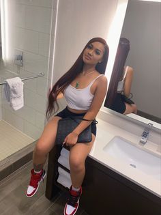 a woman sitting on top of a stool in front of a bathroom mirror next to a sink