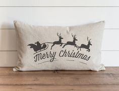 a merry christmas pillow with reindeers on it sitting on top of a wooden table