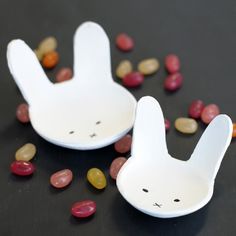 two white bunny shaped bowls sitting on top of a table next to beans and nuts