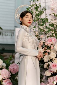 a woman wearing a white dress and hat standing in front of flowers with her hands on her hips