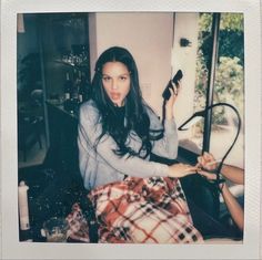 a woman sitting on top of a bed next to a window holding a cell phone