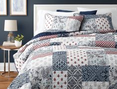 a bed with blue and white quilts in a bedroom next to a lamp on a table