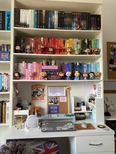 a white desk topped with lots of books next to a book shelf filled with books