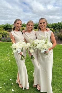 three bridesmaids in white dresses holding bouquets and posing for a photo on the grass