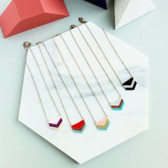 six necklaces are arranged on a white marble surface with geometric shapes in the background