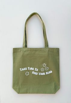 "Our Take Time to Feed Your Mind Tote makes for the perfect everyday bag. Our mission was to create functional and durable totes without sacrificing the aesthetic. To increase the functionality, we added an interior pocket so you can keep your small items right where you want them. -Can hold up to 34 lbs -Hand-printed in the US -Interior zipper pocket -Size: 15\" width by 14\" height -Strap length: 23\"" Green Canvas Tote Bag For Shopping, Everyday Green Reusable Canvas Bag, Eco-friendly Green Canvas Beach Bag, Eco-friendly Green Tote Bag, Green Tote Bags, Retro Green Tote Bag, Feed Your Mind, Minimalist Tote Bag, Green Tote Bag