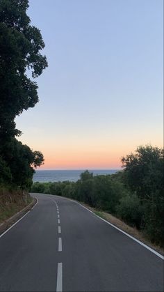 an empty road with trees and the ocean in the background