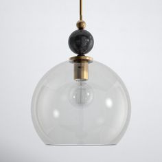 a clear glass ball hanging from a brass colored light fixture with a black marble sphere on top