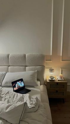 an open laptop computer sitting on top of a bed in a room with white sheets and pillows