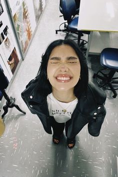 a woman with her eyes closed standing in front of desks and computer chairs, smiling at the camera